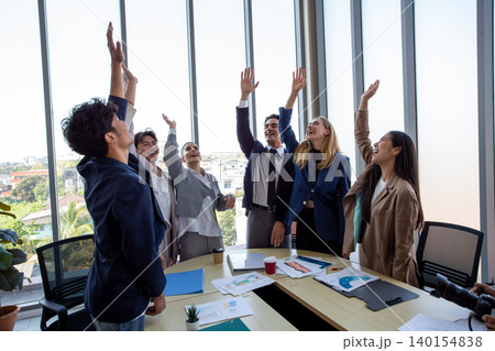 Happy business team celebrating success in office. Corporate achievement, teamwork, motivation, workplace happiness, and startup success concept. 140154838