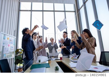 Happy business team celebrating success in office by throwing documents in the air. Corporate achievement, teamwork, motivation, workplace happiness, and startup success concept. Happy business team celebrating success in office by throwing documents in the air. Corporate achievement, teamwork, motivation, workplace happiness, and startup success concept. 140154901