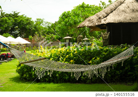 A hammock hangs between trees in a lush garden in Bali 140155516