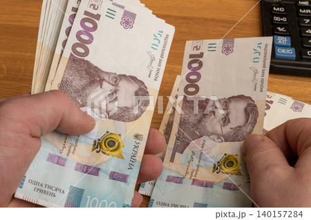 Hands counting 1000 Ukrainian hryvnia banknotes on office desk close up 140157284