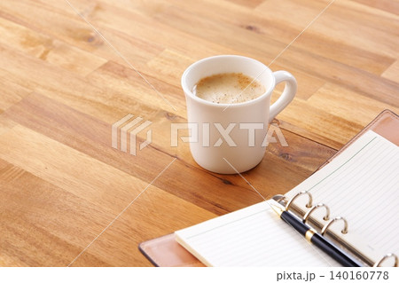 ミルクをたっぷり入れたコーヒー、カフェ・ラッテを飲みながら、システム手帳でデスクワーク中のイメージ 140160778