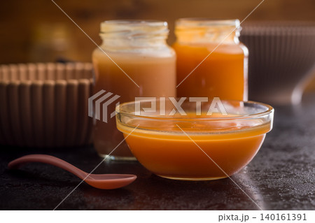 Creamy Pumpkin Soup In Glass Bowl With Jars Of Puree And Spoon On Dark Surface Creamy Pumpkin Soup In Glass Bowl With Jars Of Puree And Spoon On Dark Surface 140161391
