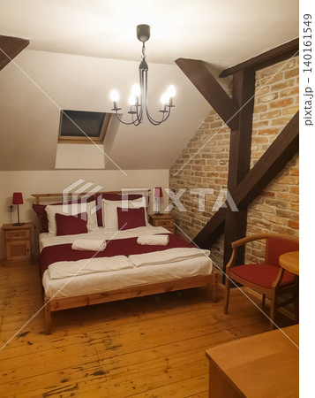 Rustic attic hotel room with exposed brick wall, wooden beams and double bed with red bedding in Prague city center Rustic attic hotel room with exposed brick wall, wooden beams and double bed with red bedding in Prague city center 140161549