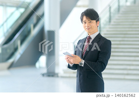 エスカレーター前でスマートフォンを見るビジネスマン エスカレーター前でスマートフォンを見るビジネスマン 140162562