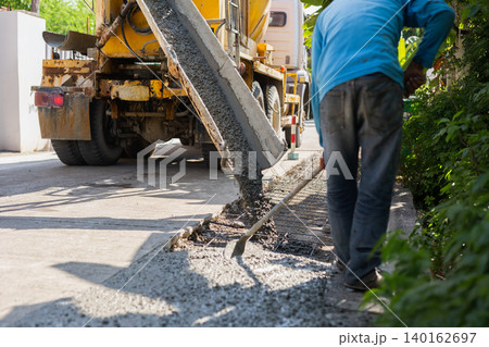 Construction worker leveling fresh wet cement pouring from a mixer truck. Construction worker leveling fresh wet cement pouring from a mixer truck. 140162697