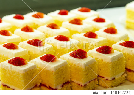 生クリームとイチゴでデコレーションした黄色いスポンジケーキの並んだ可愛らしい個別ケーキ 生クリームとイチゴでデコレーションした黄色いスポンジケーキの並んだ可愛らしい個別ケーキ 140162726