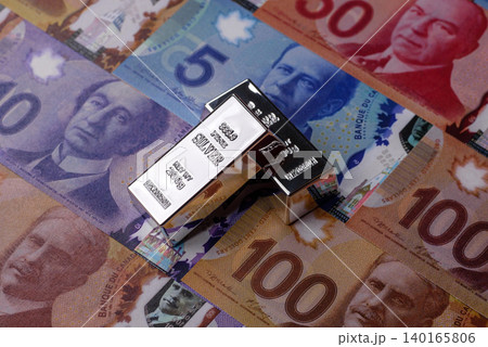 A silver bar, white metal against a backdrop of Canadian money, as a concept. A silver bar A silver bar, white metal against a backdrop of Canadian money, as a concept. A silver bar 140165806