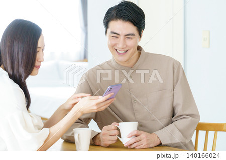 リビングでスマホとマグカップを持って微笑む若い日本人パワーカップル リビングでスマホとマグカップを持って微笑む若い日本人パワーカップル 140166024