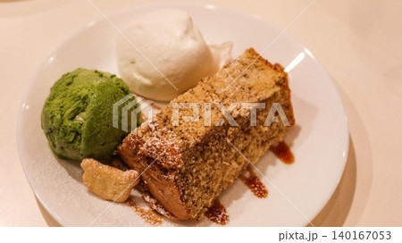 close up of earl grey sponge cake with vanilla and matcha ice cream. Syrup on the side on a white plate with copy space close up of earl grey sponge cake with vanilla and matcha ice cream. Syrup on the side on a white plate with copy space 140167053