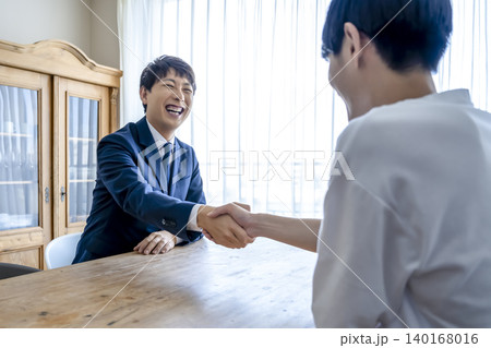 契約成立で握手を交わす営業担当者と若い男性 140168016