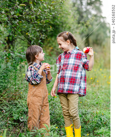 Two cheerful children gathering apples into baskets in green orchard Two cheerful children gathering apples into baskets in green orchard 140168502