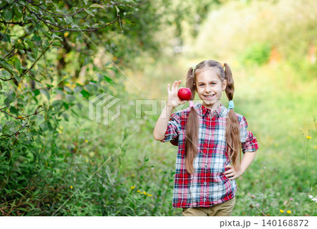 Happy girl holding red apple in orchard smiling at camera during sunny autumn day in countryside Happy girl holding red apple in orchard smiling at camera during sunny autumn day in countryside 140168872