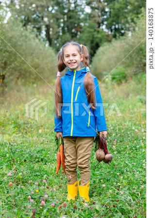 Smiling girl standing orchard holding carrots beets, wearing jacket during autumn harvest outdoors Smiling girl standing orchard holding carrots beets, wearing jacket during autumn harvest outdoors 140168875
