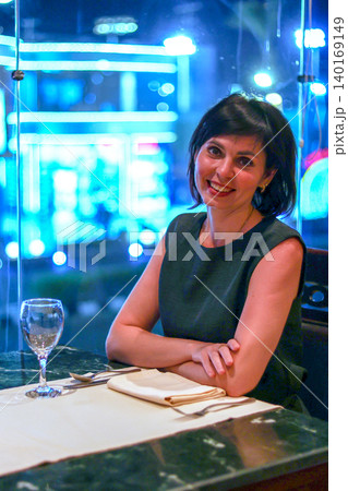 Elegant Woman Enjoying Dinner in a Restaurant with Stunning Night City View Through the Window, Capturing the Essence of Urban Sophistication 140169149