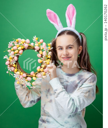 Smiling girl with bunny ears holding colorful Easter wreath with pastel eggs  140170262