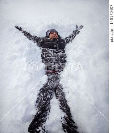 Adult man lying on fresh snow making snow angel with outstretched  140170407