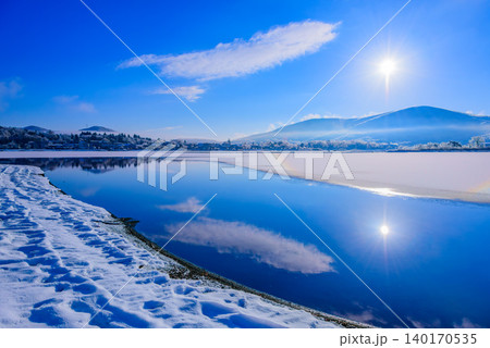 朝日に照らされる雪原の対岸と、湖面に反射する光が美しい山中湖の冬景色 朝日に照らされる雪原の対岸と、湖面に反射する光が美しい山中湖の冬景色 140170535