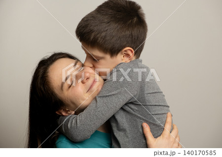 Cute school-age boy kissing his happy mother on the cheek Cute school-age boy kissing his happy mother on the cheek 140170585