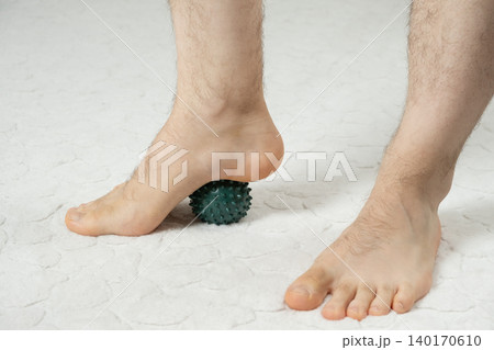 Man massaging myofascial trigger points on foot with green spiky ball 140170610