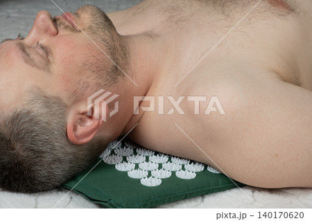 Man lying down on green acupressure mat with plastic spikes for back pain relief Man lying down on green acupressure mat with plastic spikes for back pain relief 140170620