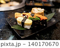 Assorted sushi platter featuring tamago nigiri, seaweed salad gunkan, fish roe gunkan, and inari sushi served on a black plate with a leaf garnish in a Japanese restaurant. Close-up food shot. 140170670