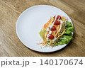 Fresh vegetable salad with shredded carrots, lettuce, and cherry tomatoes drizzled with white cream dressing on a round white plate. Served on a wooden surface. Healthy diet food concept. 140170674