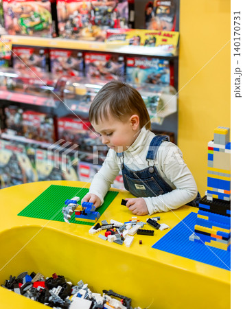 Little boy focused on assembling colorful building bricks bright table inside toy store environment 140170731