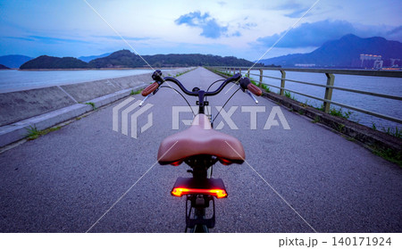 Riding a bicycle on a scenic coastal path at dusk with mountains in the background Riding a bicycle on a scenic coastal path at dusk with mountains in the background 140171924