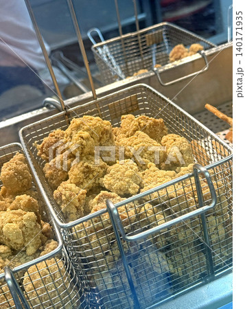 Crispy golden fried chicken pieces in metal baskets at food stall Crispy golden fried chicken pieces in metal baskets at food stall 140171935