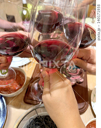 Friends clinking glasses of red wine during a celebratory dinner party 140171938