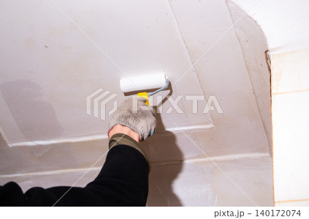 Man holding roller near freshly painted ceiling. Enjoyable weekend project. Cosmetic renovation done simply and affordably Man holding roller near freshly painted ceiling. Enjoyable weekend project. Cosmetic renovation done simply and affordably 140172074
