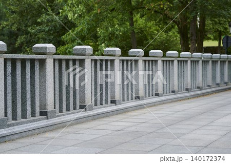 Graceful stone railing along a serene park pathway beneath lush green trees Graceful stone railing along a serene park pathway beneath lush green trees 140172374
