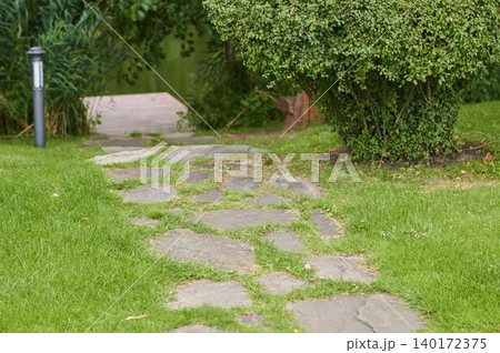Stone pathway meandering through lush greenery towards a serene garden space Stone pathway meandering through lush greenery towards a serene garden space 140172375