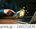 Man using smartphone with smart home security interface. Hologram icons show house shield, cloud, AI, and automation. Concept of home protection, IoT technology, and remote control via internet. 140172436