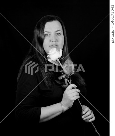 portrait of a woman looking into the camera in a dark sweater with a white rose by her face portrait of a woman looking into the camera in a dark sweater with a white rose by her face 140173043