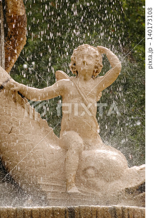 Stone sculpture of a child leaning on a fish in a fountain in El Retiro Park, Madrid, Spain.	 140173108