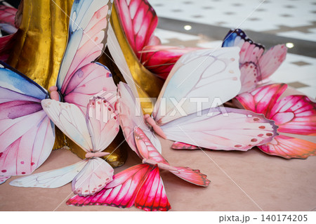 Decorative butterfly models are placed around a golden column in a shopping mall with pink white and blue wings visible on a display platform. Retail decoration and lifestyle scene Decorative butterfly models are placed around a golden column in a shopping mall with pink white and blue wings visible on a display platform. Retail decoration and lifestyle scene 140174205