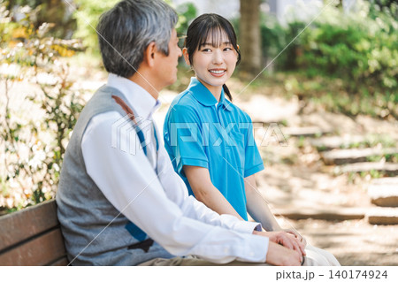 公園のベンチでシニア男性と話す介護職の若い女性 公園のベンチでシニア男性と話す介護職の若い女性 140174924