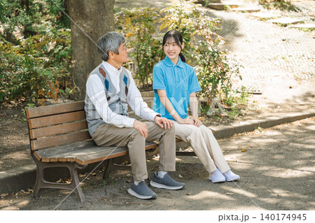 公園のベンチでシニア男性と話す介護職の若い女性 公園のベンチでシニア男性と話す介護職の若い女性 140174945