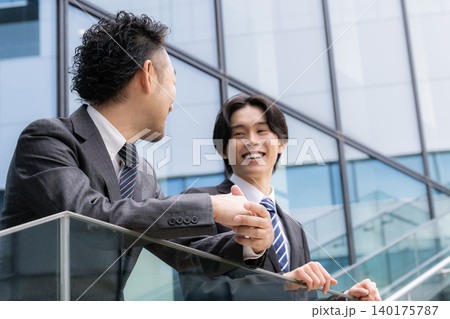 ビルの前で休憩中に話す、コミュニケーションをとる信頼関係を築きながら成長する若手社員と上司のイメージ ビルの前で休憩中に話す、コミュニケーションをとる信頼関係を築きながら成長する若手社員と上司のイメージ 140175787