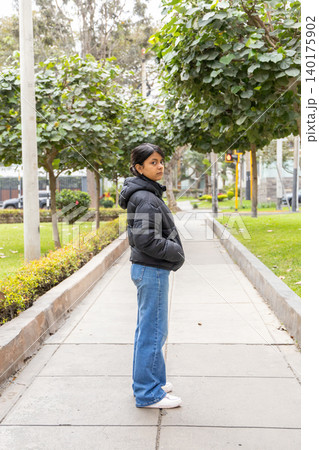 A teenager in a black jacket and blue jeans stands in front of a gate A teenager in a black jacket and blue jeans stands in front of a gate 140175902