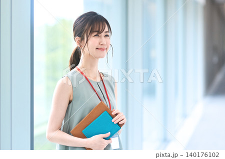 社員証と手帳を抱え遠くを見つめ微笑むビジネスウーマン 社員証と手帳を抱え遠くを見つめ微笑むビジネスウーマン 140176102