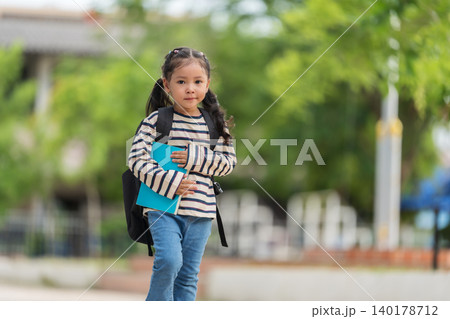 happy student carrying a schoolbag and holding a book while walking to school on the first day of semester. 140178712