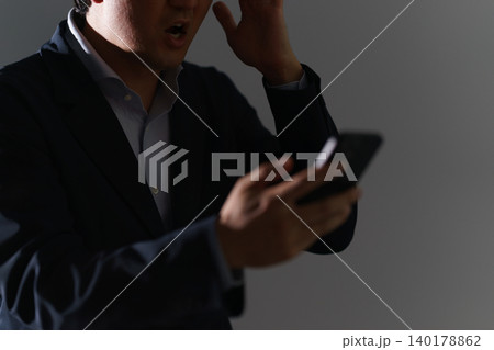 暗い室内でスマートフォンを前に頭を抱え犯罪被害に遭った30代スーツ姿の顔無しの男性 暗い室内でスマートフォンを前に頭を抱え犯罪被害に遭った30代スーツ姿の顔無しの男性 140178862