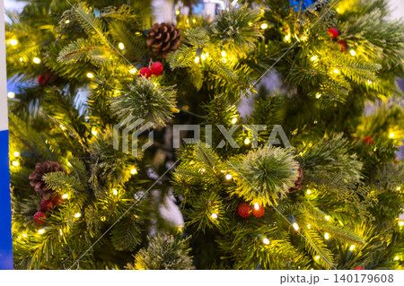 close up of a green christmas tree decorated with small warm lights pine cones and red berries close up of a green christmas tree decorated with small warm lights pine cones and red berries 140179608
