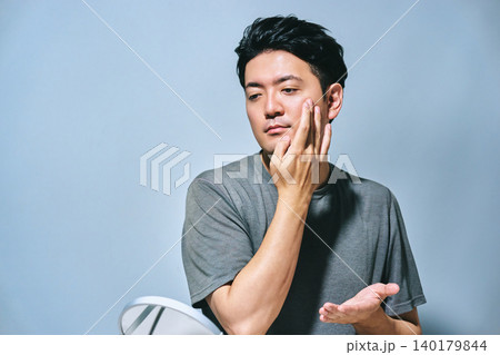 鏡を見て頬に手を当てて肌のケアをする30代の日本人男性の紫外線や日焼け対策の夏イメージ 140179844