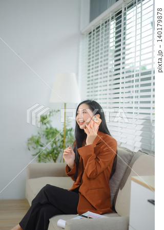 Asian businesswoman reading paperwork on sofa in modern home office, professional corporate lifestyle 140179878
