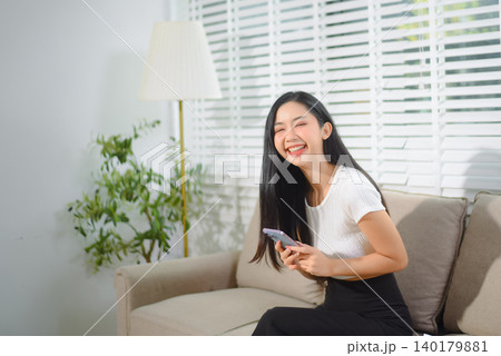 Asian businesswoman working from home on a cozy sofa, reviewing documents in a modern living room with a comfortable remote work lifestyle vibe. Asian businesswoman working from home on a cozy sofa, reviewing documents in a modern living room with a comfortable remote work lifestyle vibe. 140179881