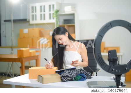 Young Asian women selling clothes on video streaming.Startup small business SME, using smartphone or tablet Young Asian women selling clothes on video streaming.Startup small business SME, using smartphone or tablet 140179944
