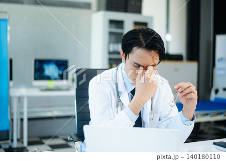 Asian doctors look stressed while reviewing patient results on laptops in a modern hospital clinic. Concept of medical pressure, diagnosis, and healthcare 140180110